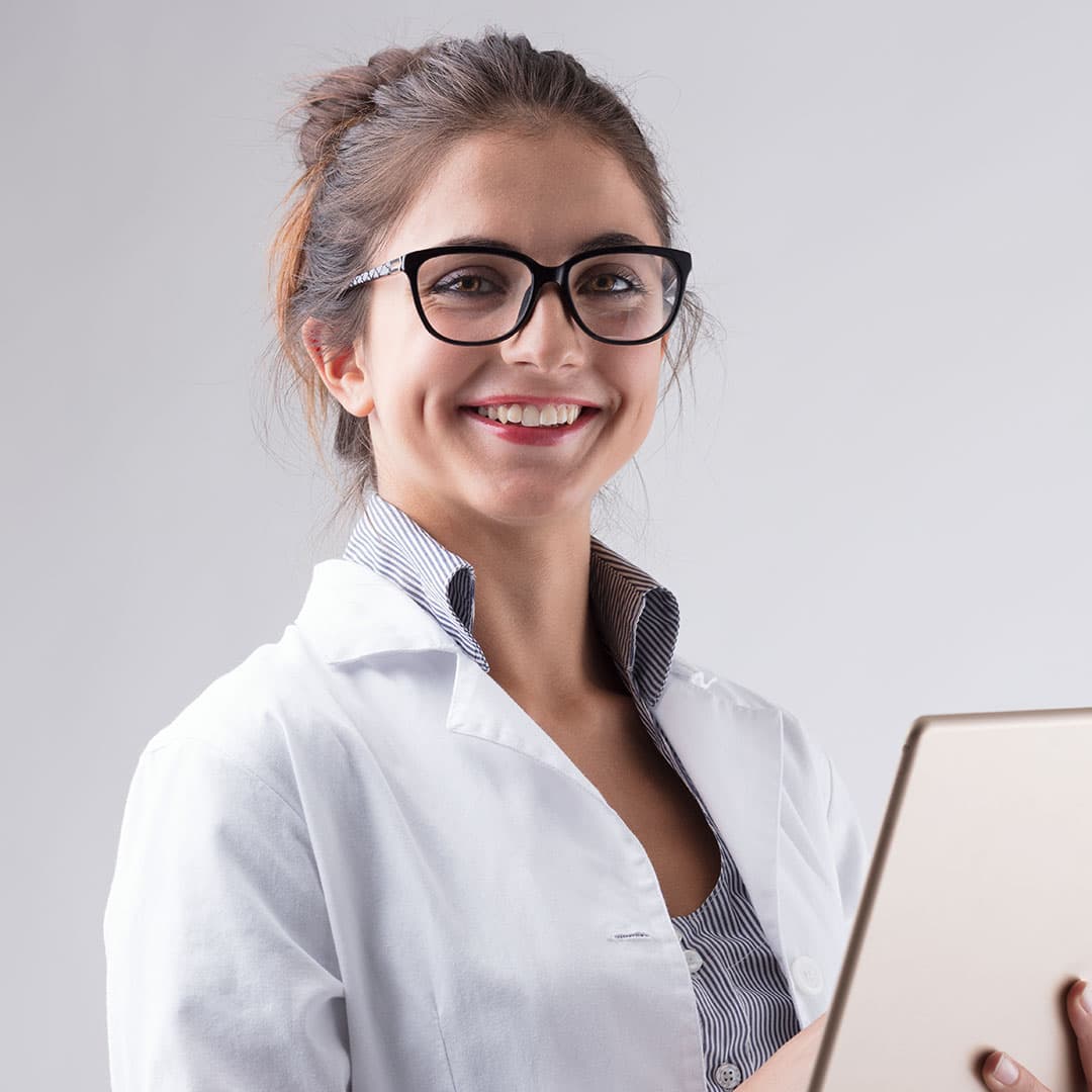 A woman with glasses and brown hair in a bun wears a lab coat and holds a clipboard.