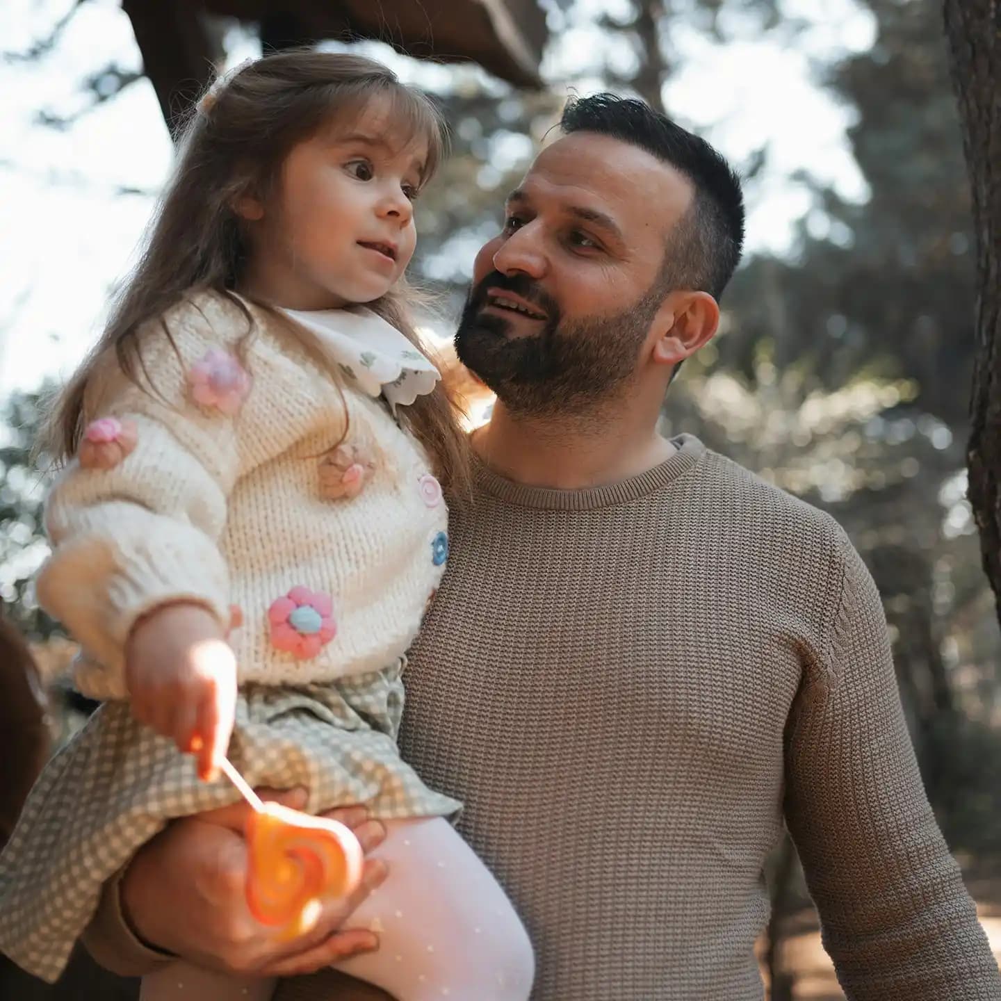 A father holding his daughter in one arm in a nature background. 