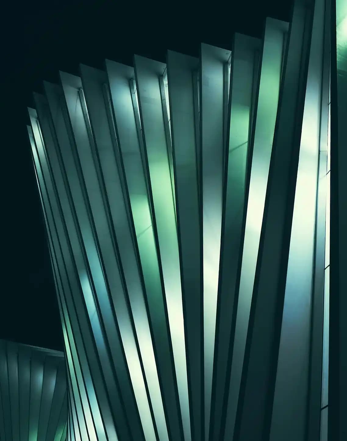 Tall teal panels stand in a curved formation, illuminated with light that enhances their reflective surfaces.